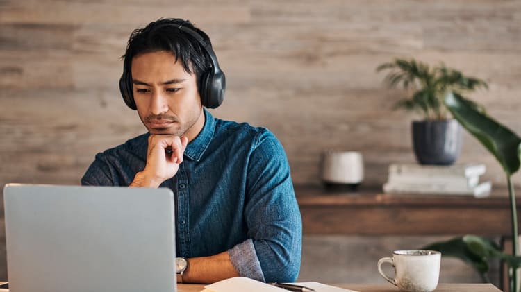 A man wearing headphones is working on a laptop.