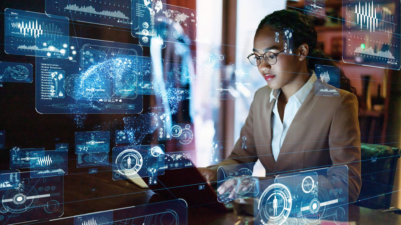 A woman is working on a laptop in front of a digital screen.