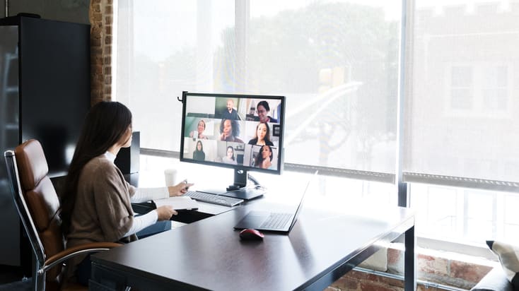 A woman sits at a desk and uses a video conferencing system.