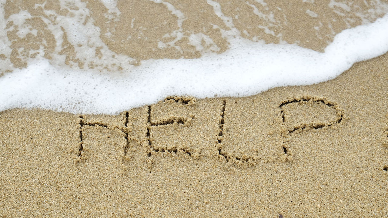 The word help written in the sand on a beach.