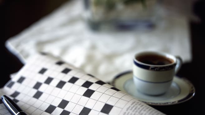 A cup of coffee and a crossword puzzle on a table.