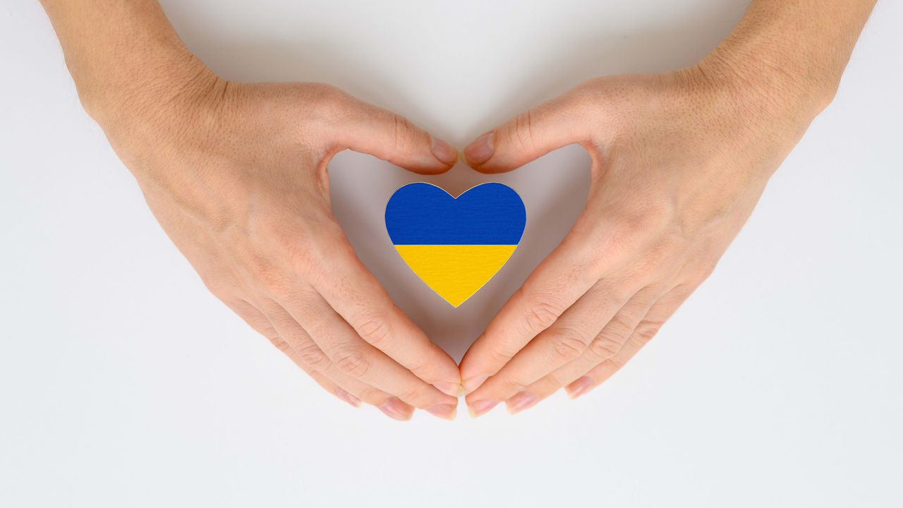 A woman's hands make a heart shape with the flag of ukraine.