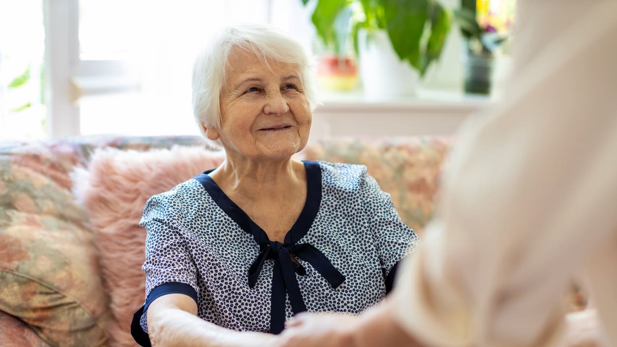 An elderly woman shakes hands with a caregiver.