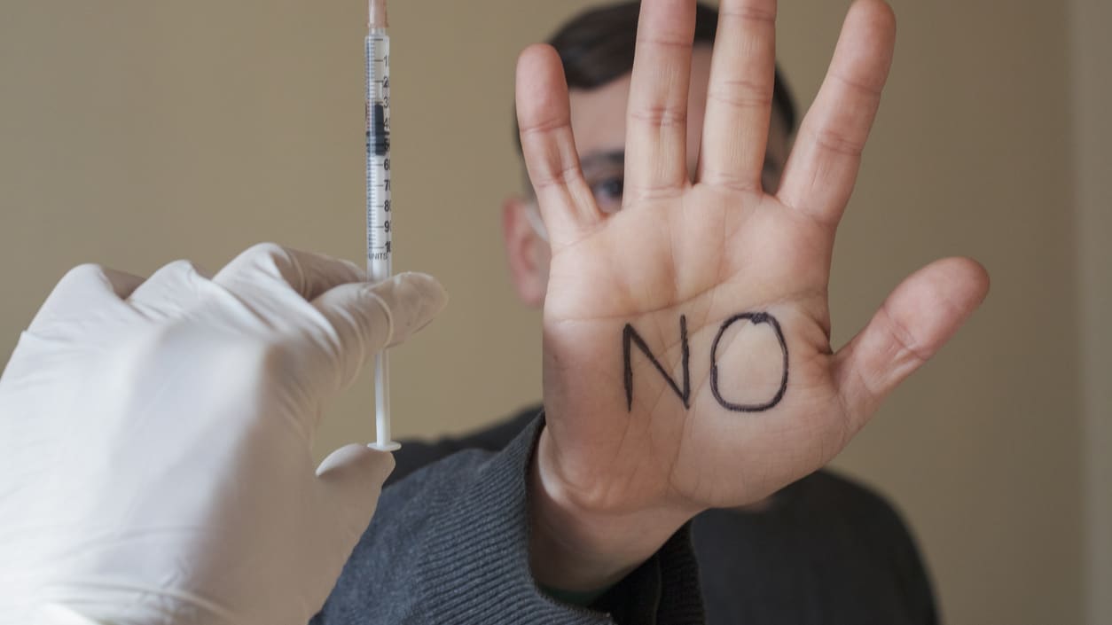 A syringe held up next to a man's hand with the word no written on it.
