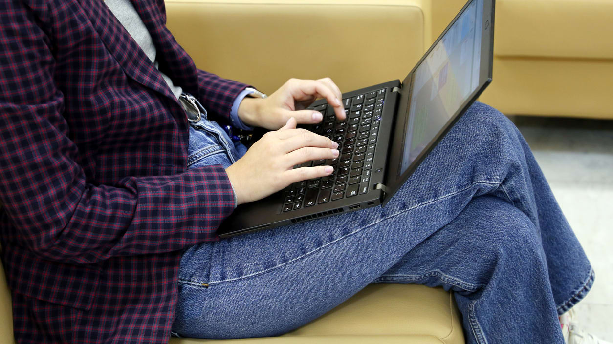 A woman sitting on a couch typing on a laptop.