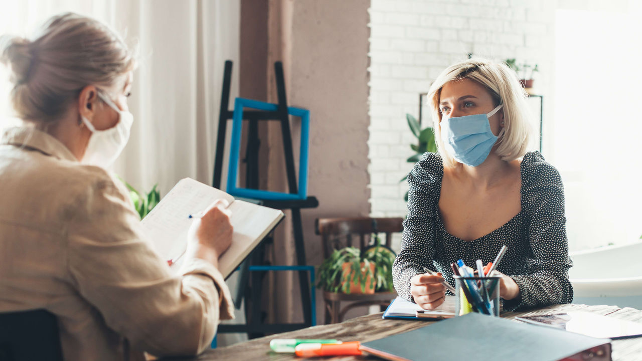 Two women wearing surgical masks at a table.