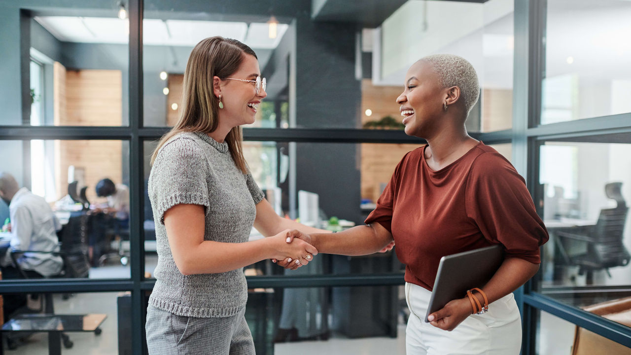 Two business women shaking hands in an office.