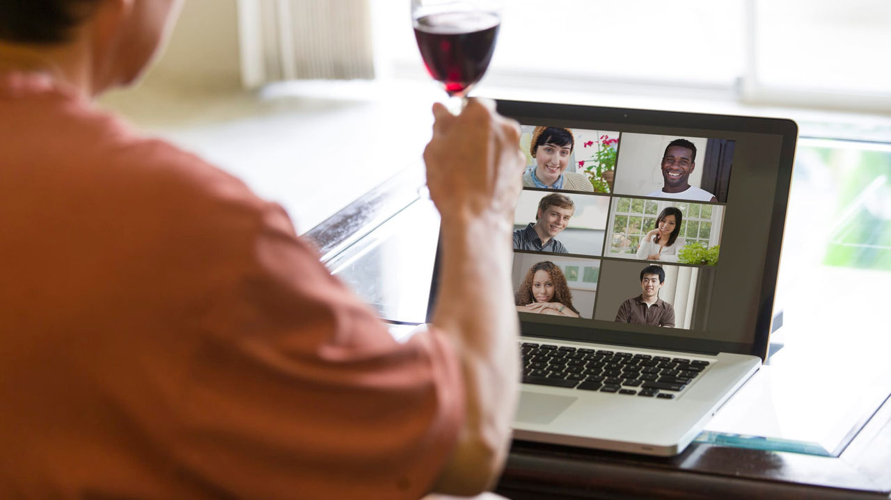 A man holding a glass of wine on a laptop.