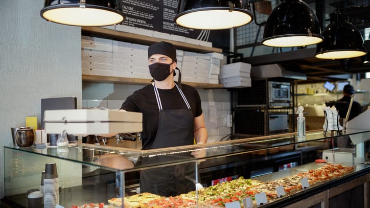 A pizza chef wearing a mask in front of a counter.