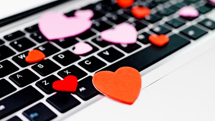 Red and pink foam cutout hearts scattered on a laptop keyboard.
