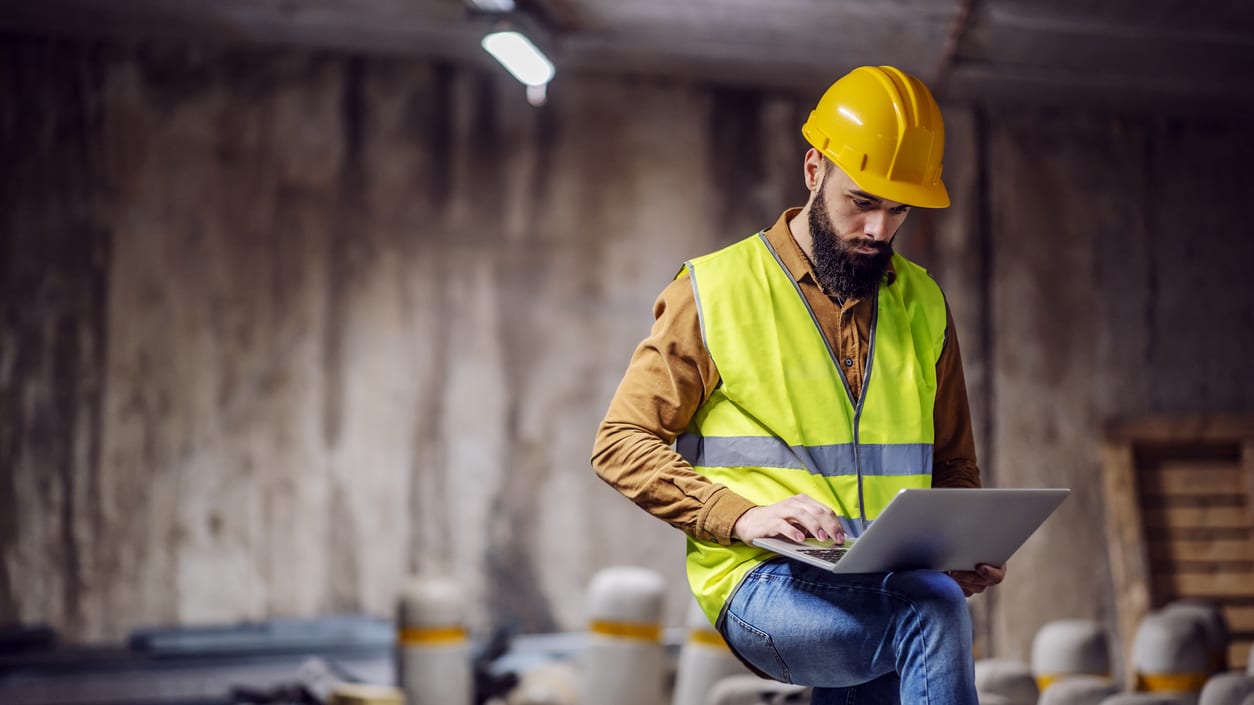 A construction worker using a laptop in a construction site.