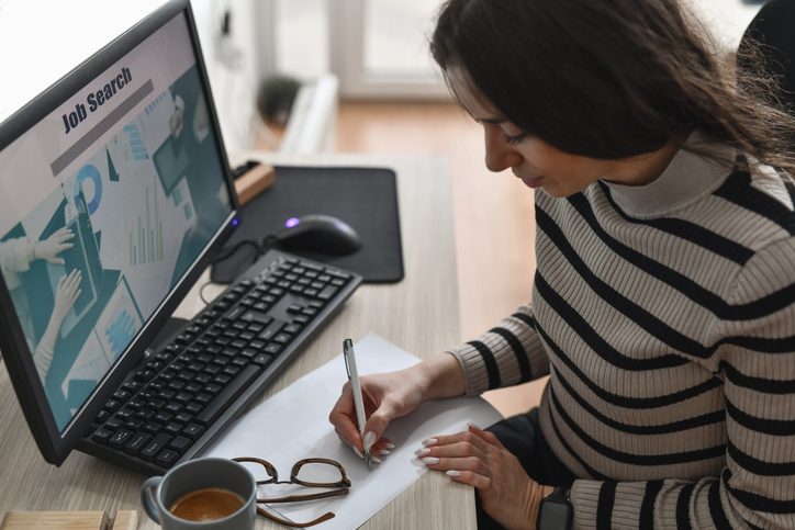 Person taking notes by a computer during a job search.