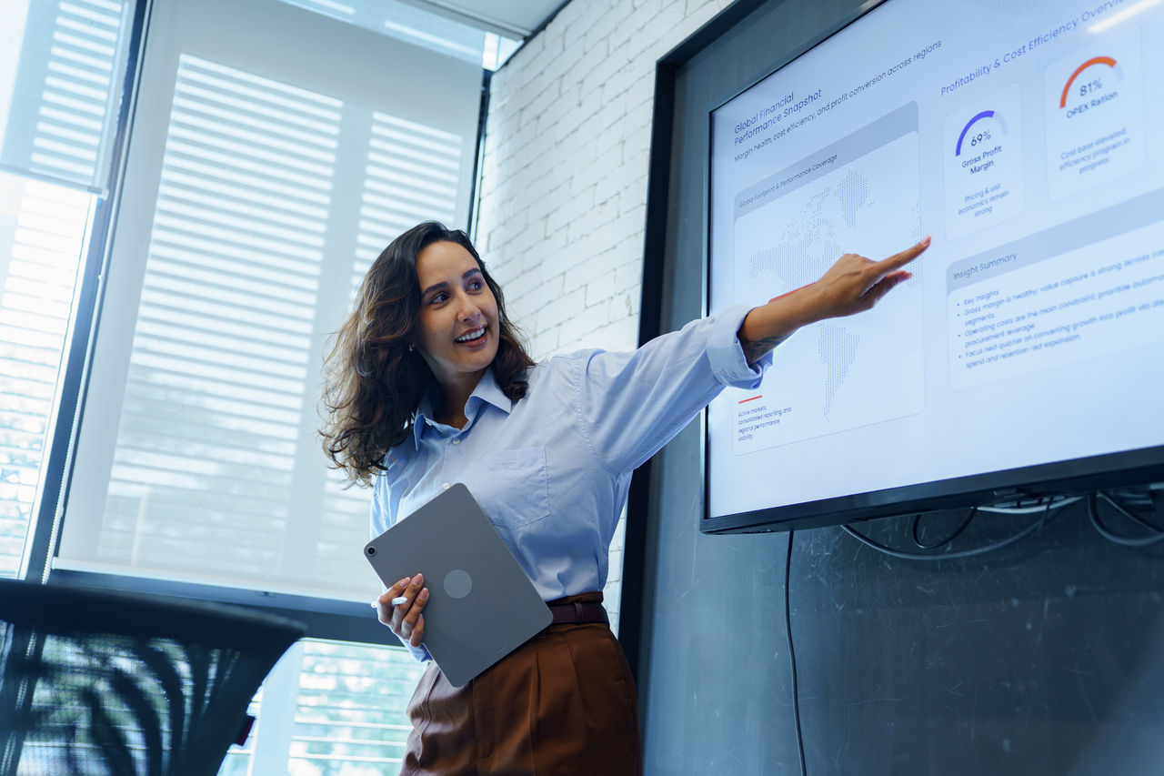 Businesswoman Leading Team Presentation with Charts and Report Screen in Modern Office Meeting Room.