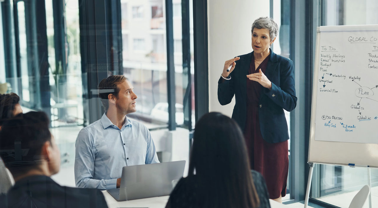Meeting, whiteboard and senior business woman in boardroom with team for training or coaching. Presentation, planning or strategy with manager and employee group in office for upskill development