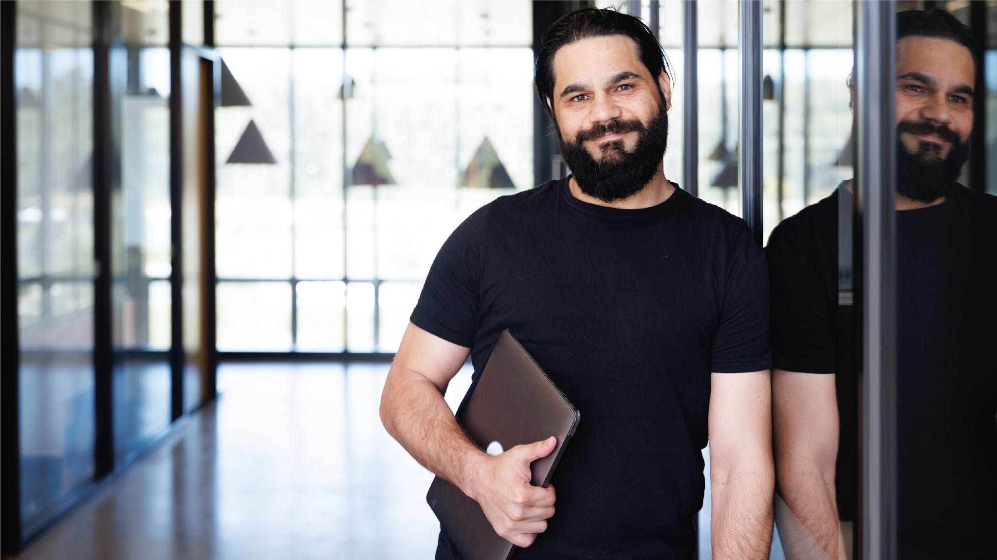 Employee smiles at the camera with his laptop. 