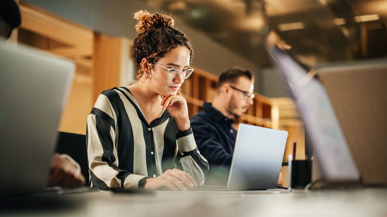 1481370371 Portrait of Enthusiastic Hispanic Young Woman Working on Computer in a Modern Bright Office. Confident Human Resources Agent Smiling Happily While Collaborating Online with Colleagues.