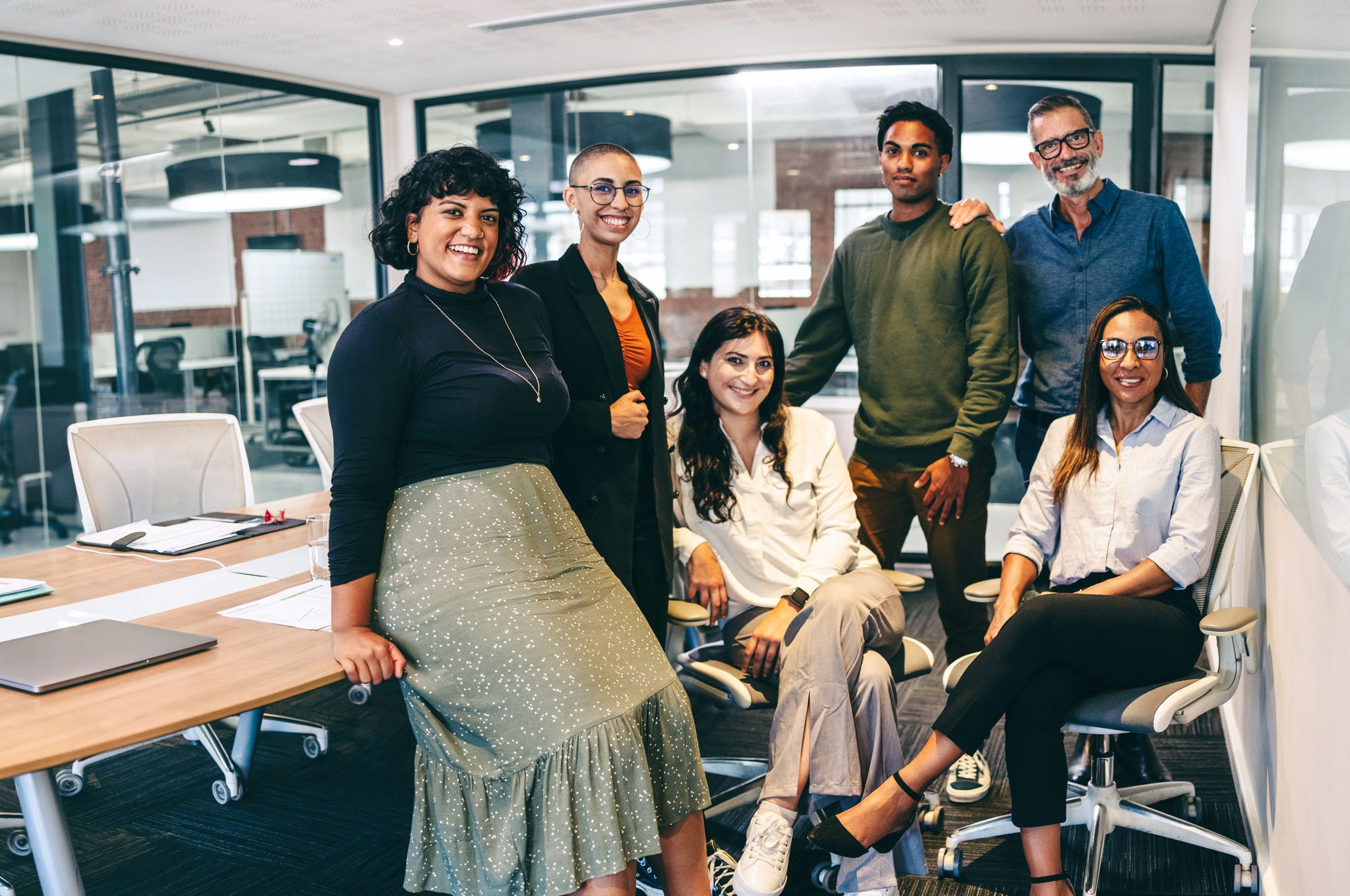 1366793164 Team of businesspeople smiling at the camera in a boardroom. Cheerful businesspeople grouped together in a modern workplace. Diverse team of businesspeople looking cheerful.