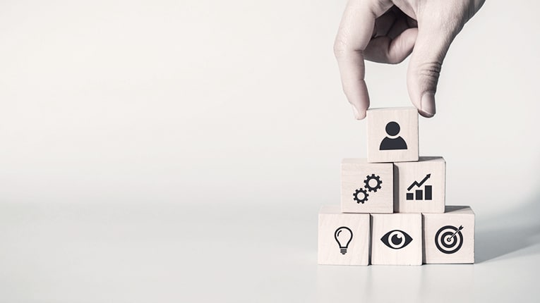 A hand is holding wooden blocks with business icons on them.