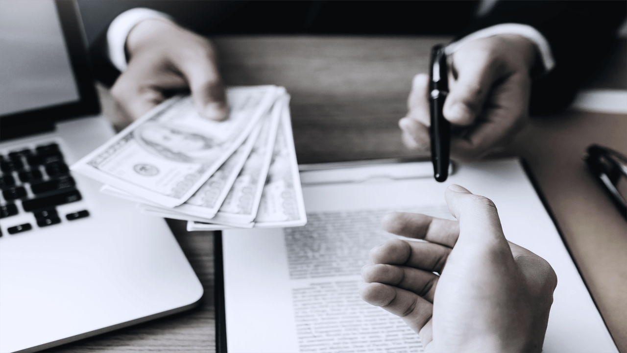 A person is handing money to another person at a desk.