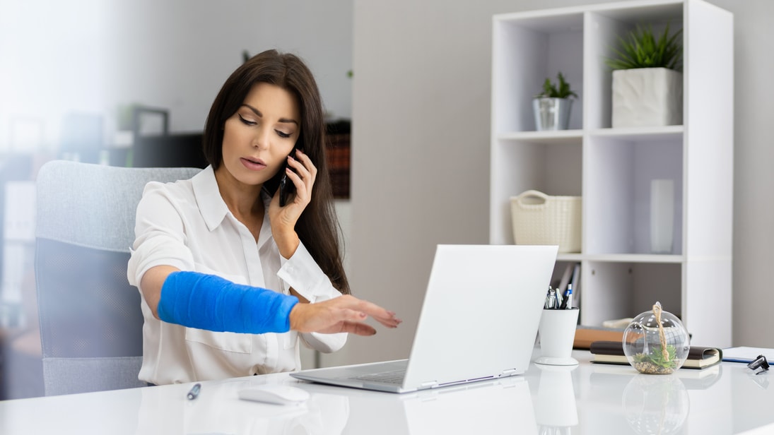 A woman with a blue bandage on her arm is working on her laptop.