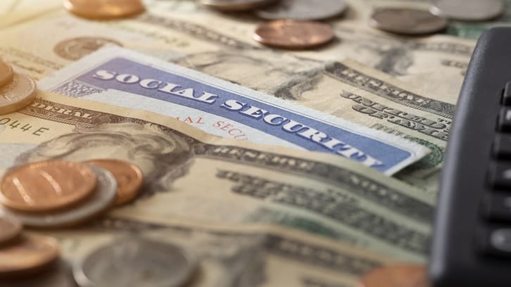 A social security card on top of a pile of money and a calculator.
