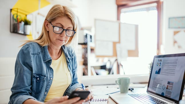 A woman sitting at a desk with a laptop and cell phone.