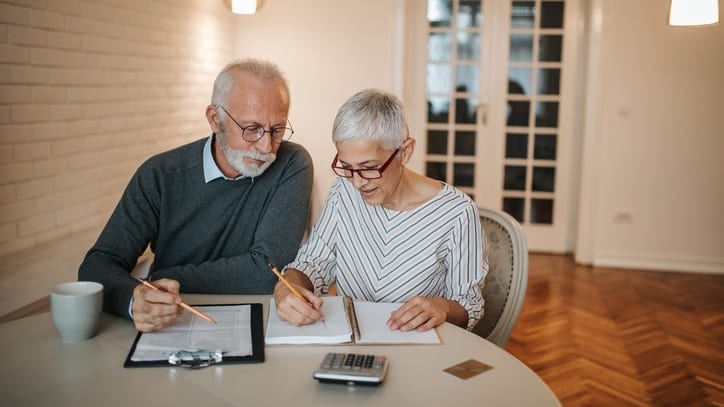 An older couple sitting at a table and writing on a piece of paper.