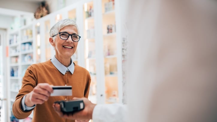 A woman is handing over a credit card to a man in a pharmacy.