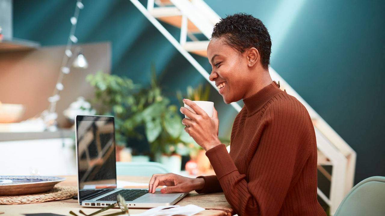 A woman sitting at a table with a laptop and a cup of coffee.