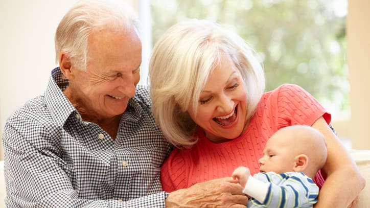 An elderly couple holding a baby on a couch.