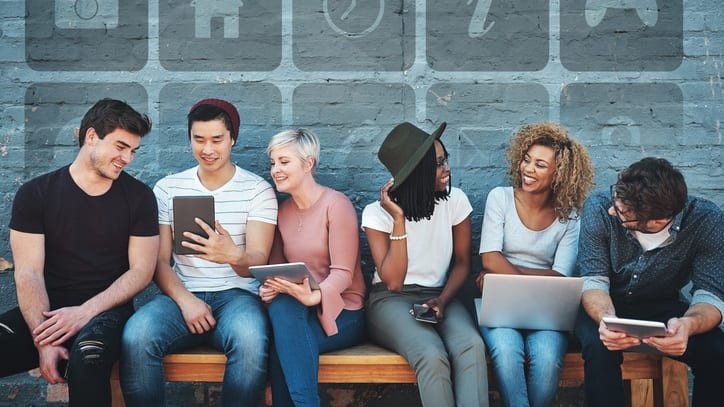 A group of people sitting on a bench looking at their phones.