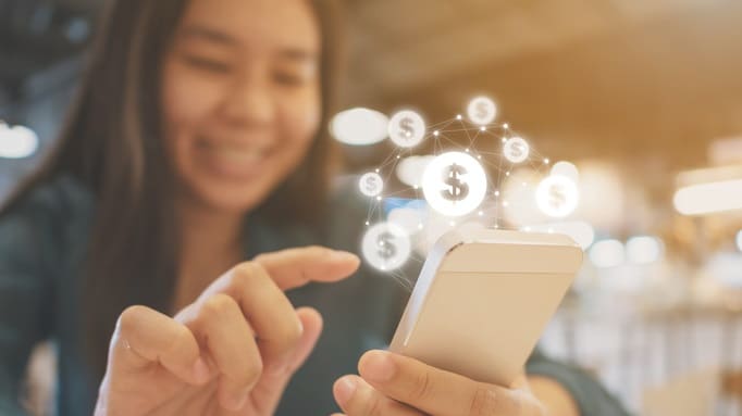 A woman using a smartphone with money coming out of it.