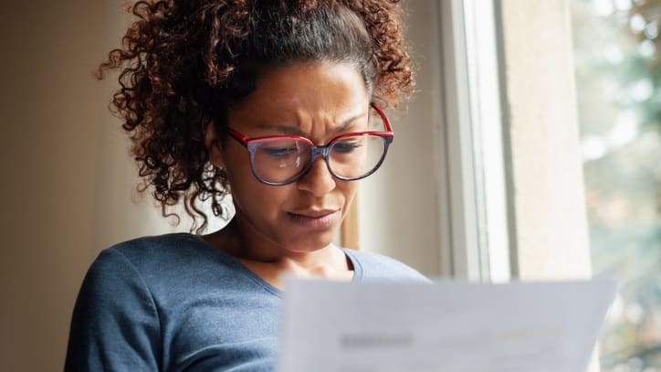 A woman is looking at a piece of paper in front of a window.