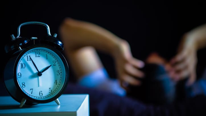 A person laying on a bed with an alarm clock.