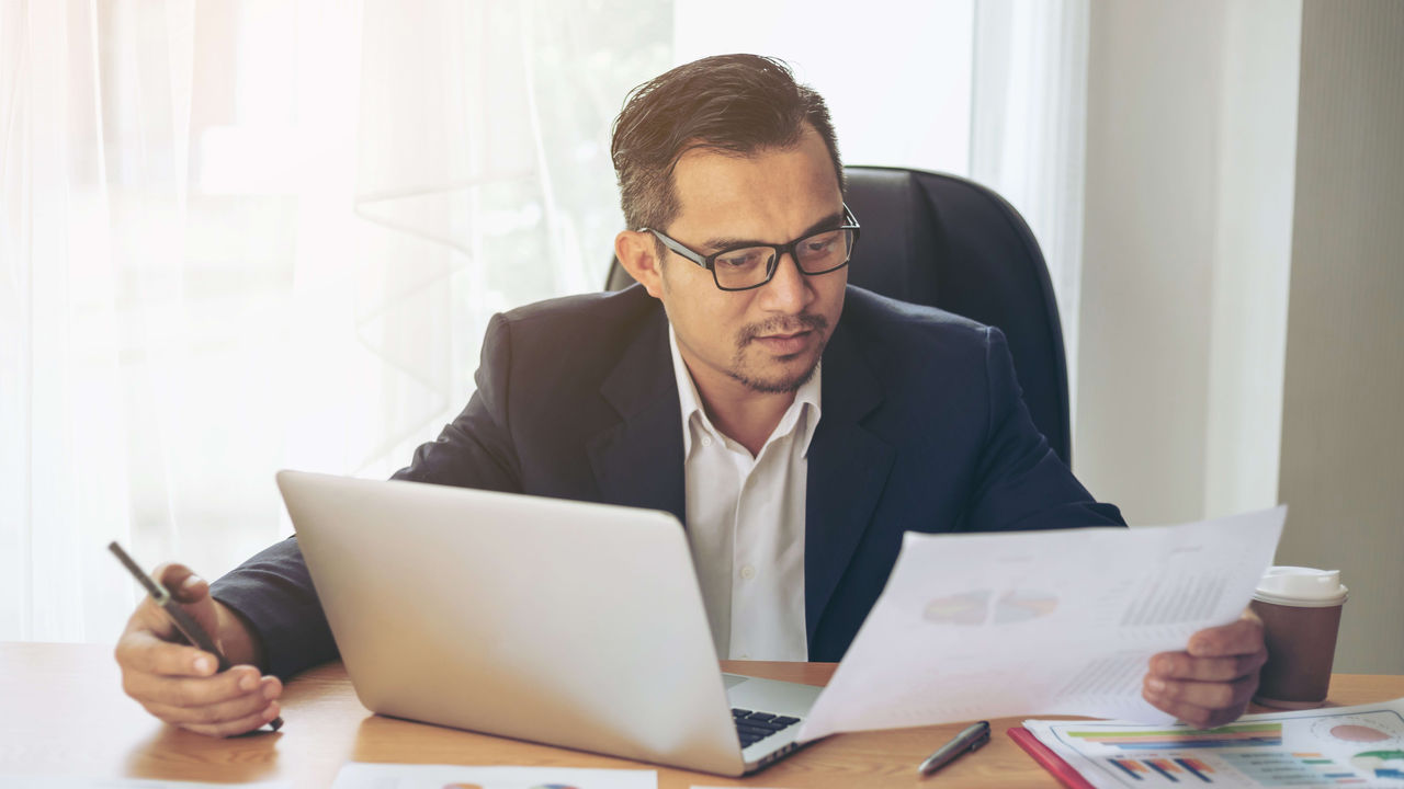 A businessman sitting at a desk with papers and a laptop.