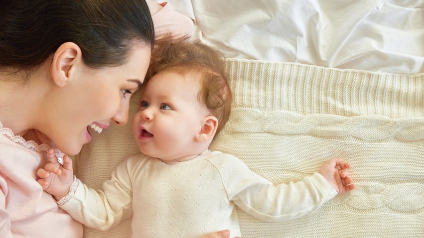 A woman laying on a bed with her baby.