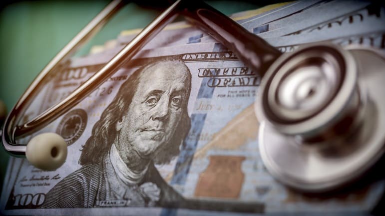 A stethoscope sits on top of a stack of money.