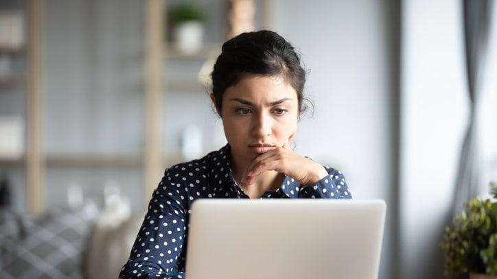 A woman sitting at a table looking at her laptop.