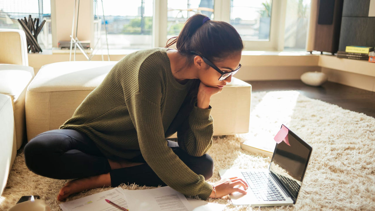 A woman sitting on the floor with a laptop and papers.