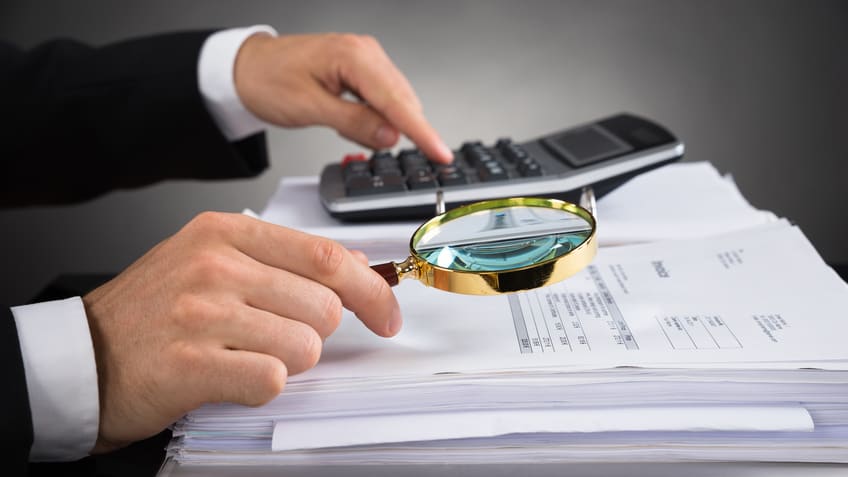 A man in a suit is holding a magnifying glass and a calculator.
