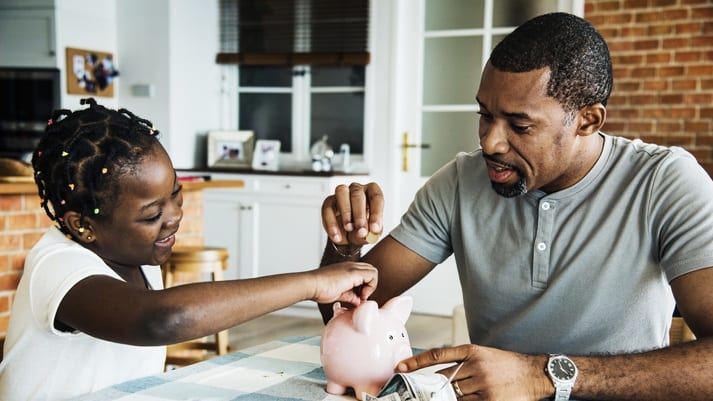 A man and his daughter putting money into a piggy bank.