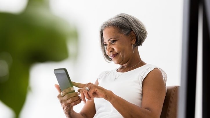 An older woman sitting in a chair looking at her phone.