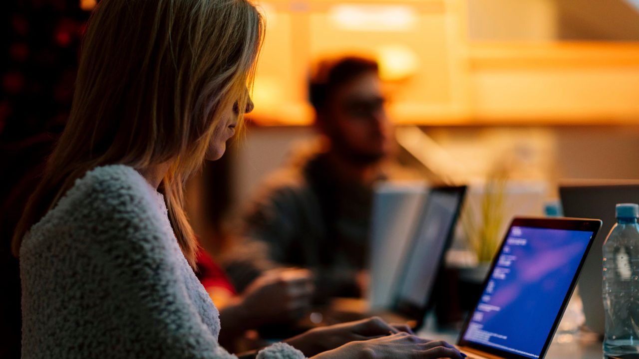 A woman is working on a laptop in front of a group of people.