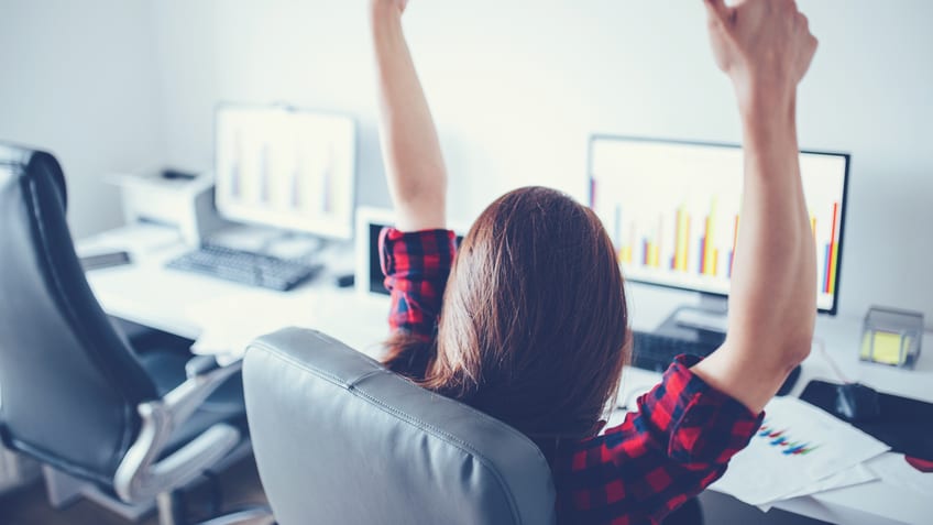 A woman raising her arms in front of a computer screen.