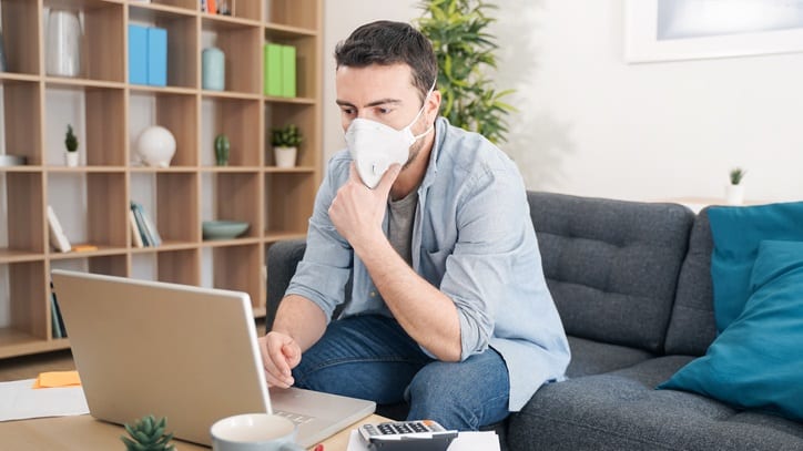 A man wearing a face mask while working on his laptop at home.