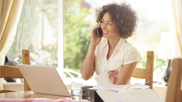 A woman talking on the phone while sitting at a table with a laptop.