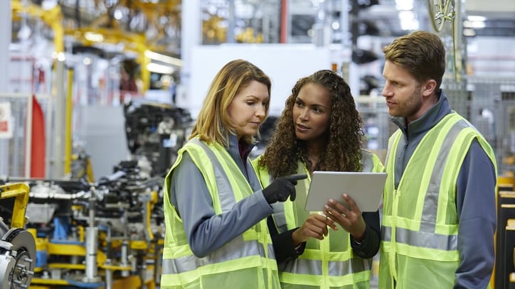 Three workers in a factory looking at a tablet.