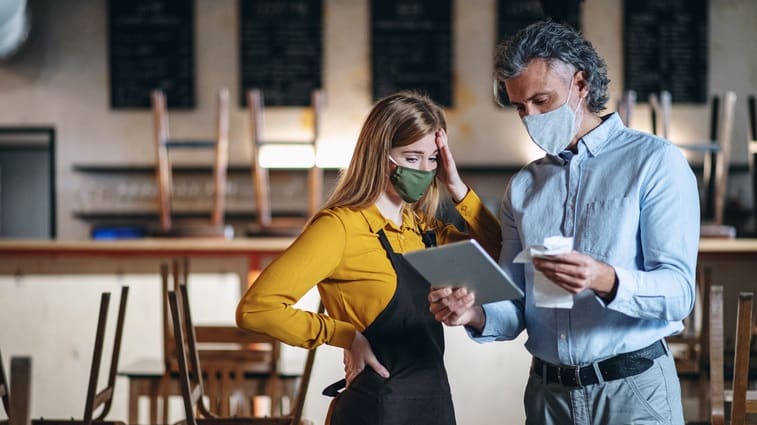 A man and woman wearing face masks are standing in a restaurant.