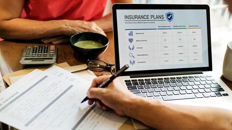 A man and woman looking at a laptop with an insurance plan on it.