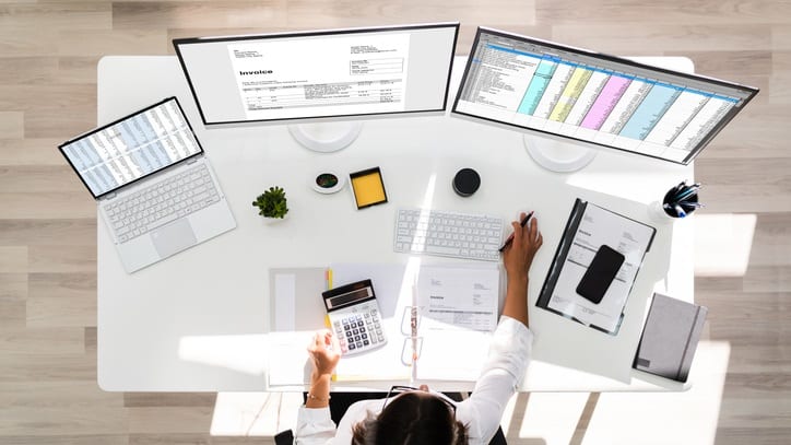 A woman working at a desk with two monitors and a calculator.